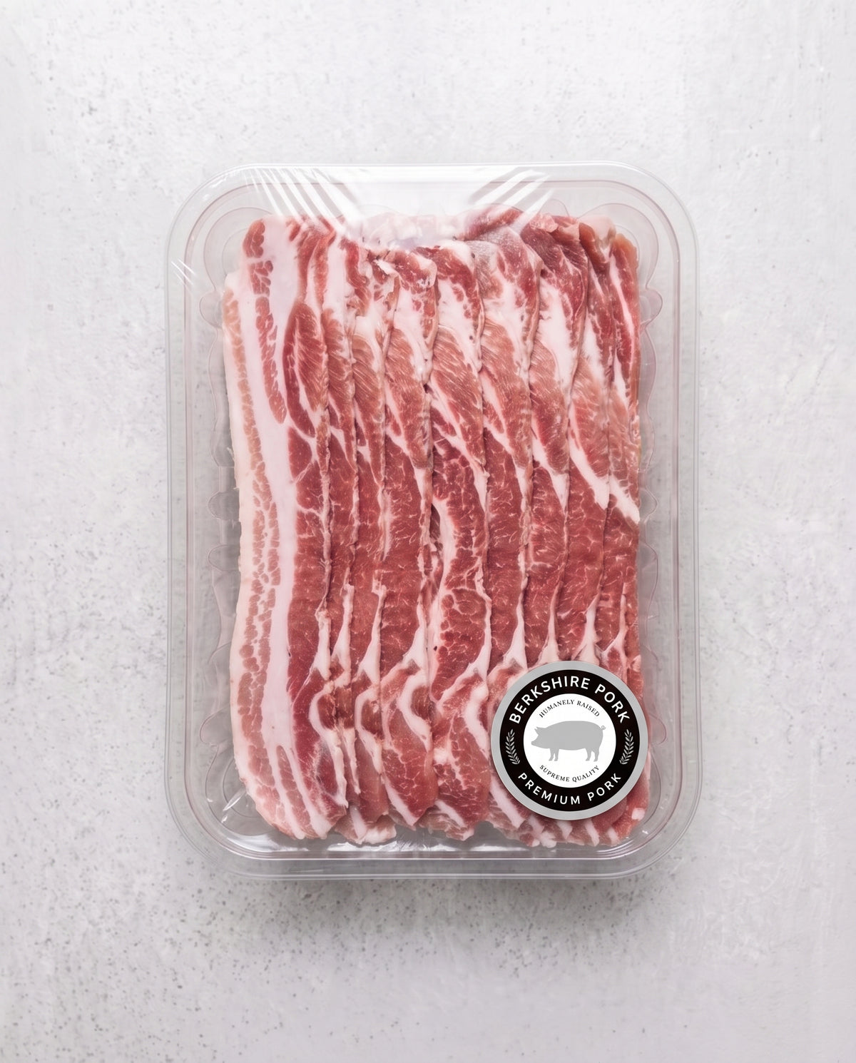 A plastic container filled with fresh, thinly sliced Berkshire pork belly strips showing distinct layers of red meat and white fat, labeled with a circular Berkshire Pork seal.